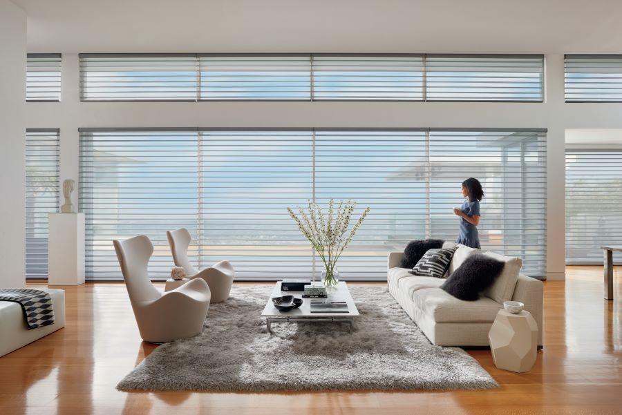 A woman looking out her living room windows. Sheer Hunter Douglas blinds cover the large picture windows.