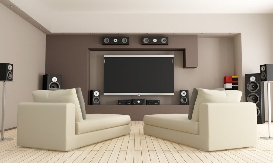 A living room featuring a home theater system, surround sound speakers, and comfy seating.
