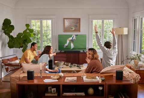 Friends watch TV in a living room with cozy seating, plants, and ambient lighting, creating a warm setting for entertainment.