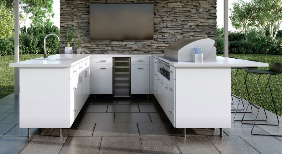 A U-shaped white outdoor kitchen with a grill and a TV on a rock wall.