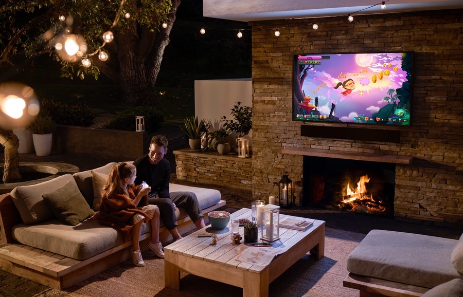 Father and daughter watching a cartoon on an outdoor TV on a patio at night.