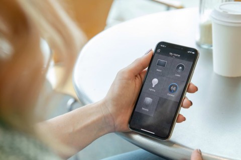 Woman’s hand holding a smart phone displaying the interface for a Control4 home automation system.