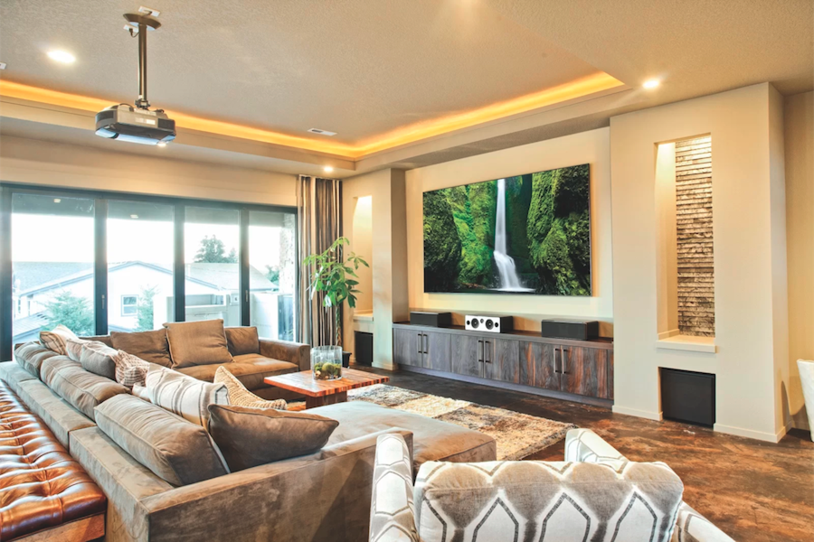 Gray couch in a media room facing a projected image of a waterfall with windows in background showing a neighboring home.