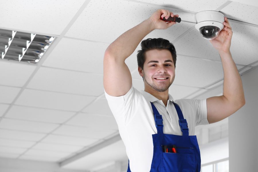 A worker installing a security camera on a ceiling.