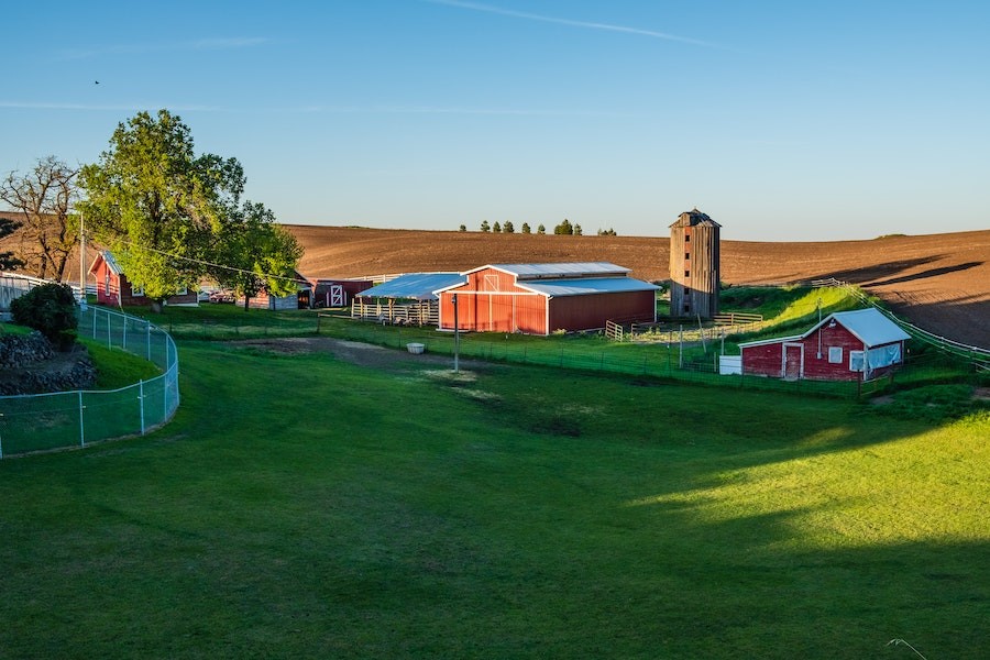 Red barn buildings with a silo and rolling hills in the background.